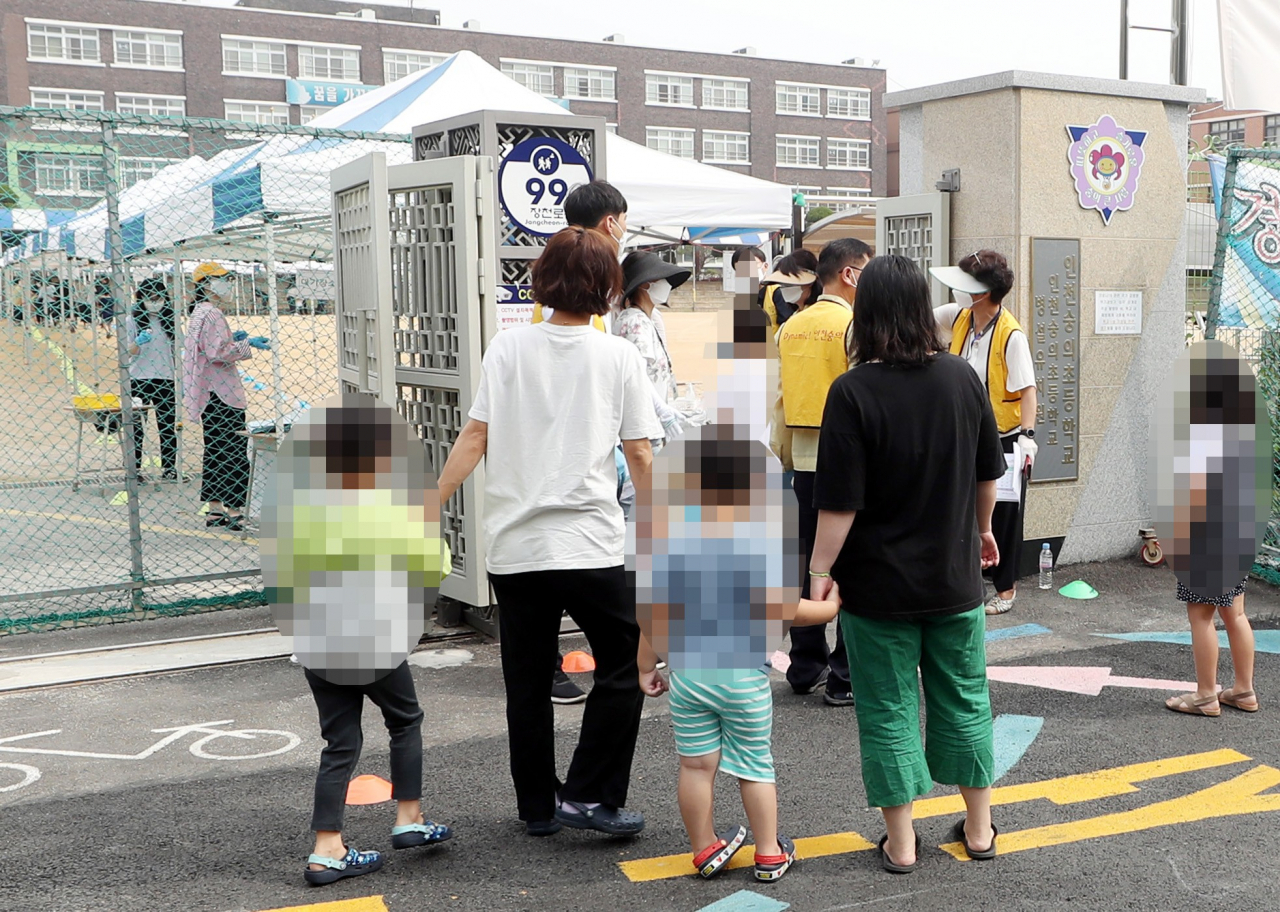 인천지역에 신종 코로나바이러스 감염증(코로나19) 확진자가 속출한 17일 오전 확진자가 나온 인천시 미추홀구 한 초등학교 정문에 검체 검사를 받으러 온 학생들이 부모와 함께 줄지어 서 있다. [연합]