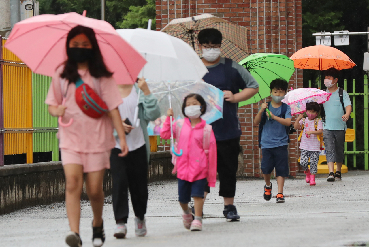 광주·전남지역에 비가 내린 18일 오전 광주 북구 오치초등학교에서 학생들과 병설유치원생들이 마스크를 쓰고 코로나19 예방 발열체크를 하기 위해 줄지어 이동하고 있다. [연합]