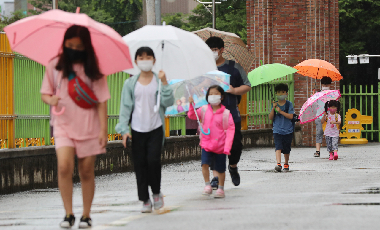 광주·전남지역에 비가 내린 18일 오전 광주 북구 오치초등학교에서 학생들과 병설유치원생들이 마스크를 쓰고 코로나19 예방 발열체크를 하기 위해 줄지어 이동하고 있다. [연합]