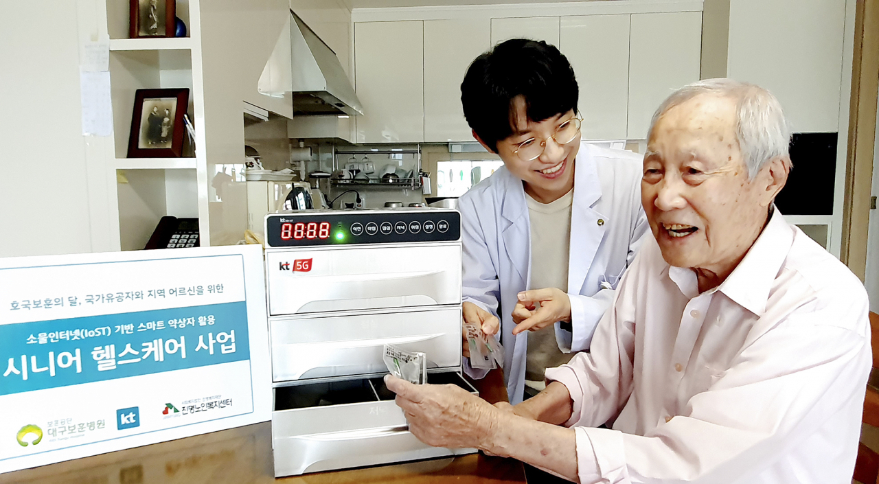 KT가 한국전쟁 70주년과 호국보훈의 달을 맞아 국가유공자를 대상으로 ICT 헬스케어 솔루션을 지원했다고 22일 밝혔다. 사진은 대구 보훈병원 방문간호사가 국가유공자 김갑생 씨의 자택에서 스마트 약상자를 이용해 복약 지도를 하고 있는 모습. [KT 제공]