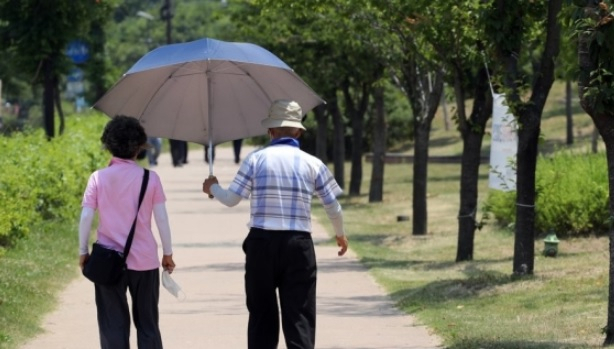 서울 지역에 폭염주의보가 발령된 지난 22일 서울 영등포구 여의도 한강공원에서 한 노부부가 우산을 쓰고 걸어가고 있다. 남편 어깨 반은 햇볕에 나와 있다. [연합]