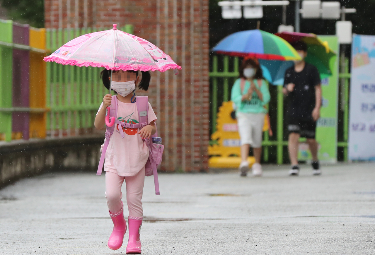 광주·전남 지역에 비가 내린 지난 18일 오전 광주 북구 오치초등학교·병설유치원에서 학생들이 마스크를 쓰고 우산을 든 채 발열 체크하기 위해 이동하고 있다. [연합]