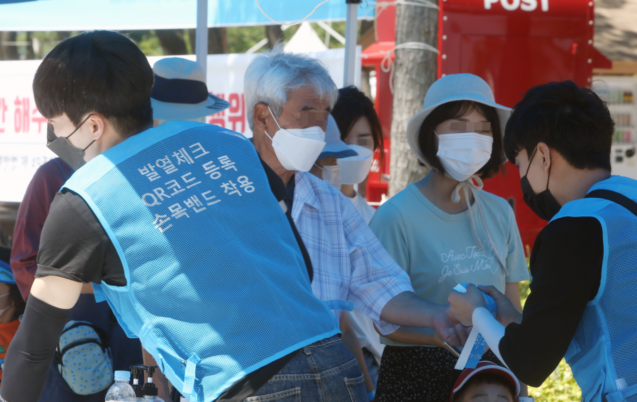 17일 개장한 강원도 강릉시 경포해수욕장에서 통제 요원들이 피서객을 대상으로 QR코드를 등록한 뒤 손목 밴드를 부착해주고 있다. [연합]