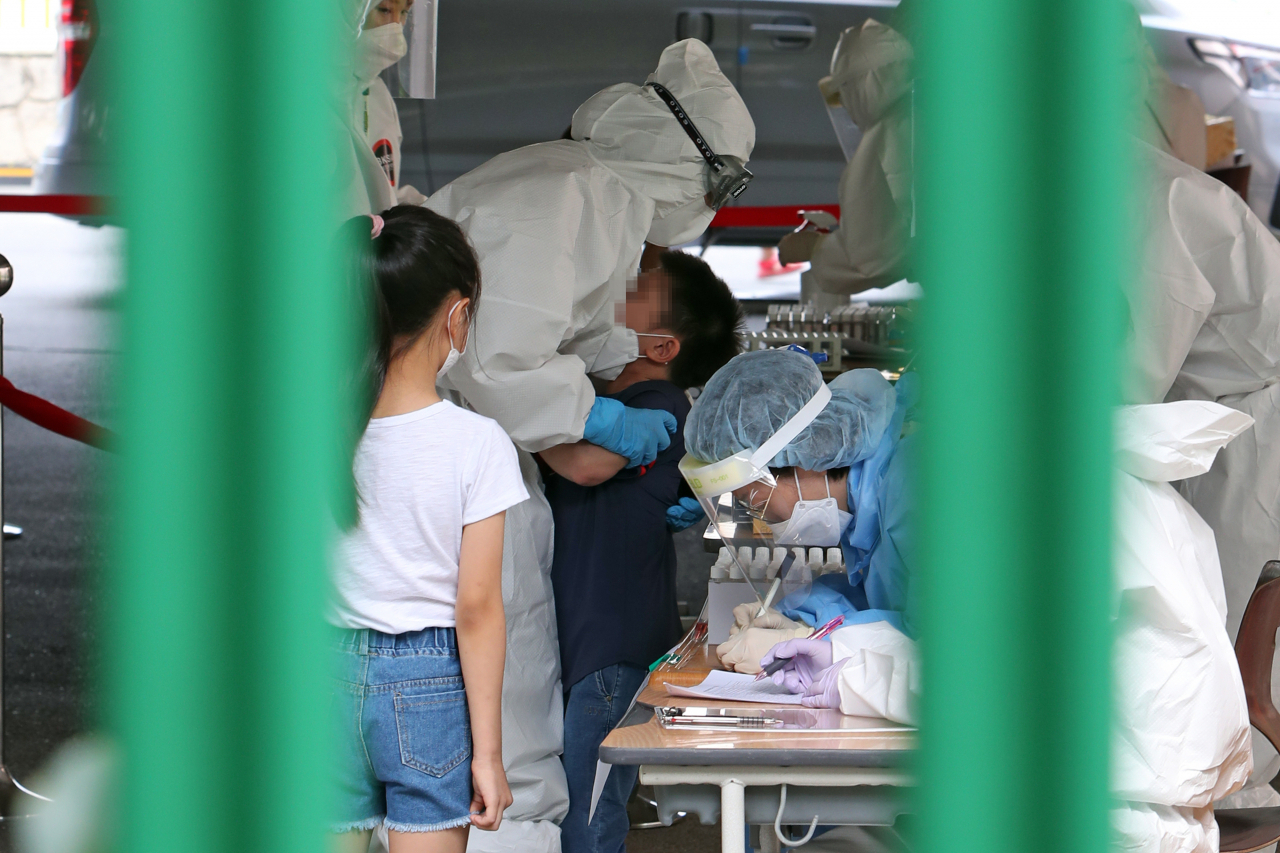 [사진=18일 오후 광주 서구 치평동 계수초등학교 주차장에 마련된 이동선별진료소에서 의료진이 울음을 터뜨리는 아이를 달래고 있다. 방역 당국은 재학생인 남매가 코로나19 확진 판정을 받아 계수초 전교생에 대해 전수검사를 하기로 했다.] [연합]