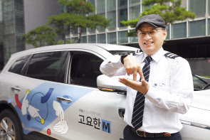 청각장애인 기사님이 ‘고요한M’차량 앞에서 ‘자립’이라는 의미의 수어를 하고 있는 모습.[SK텔레콤 제공]