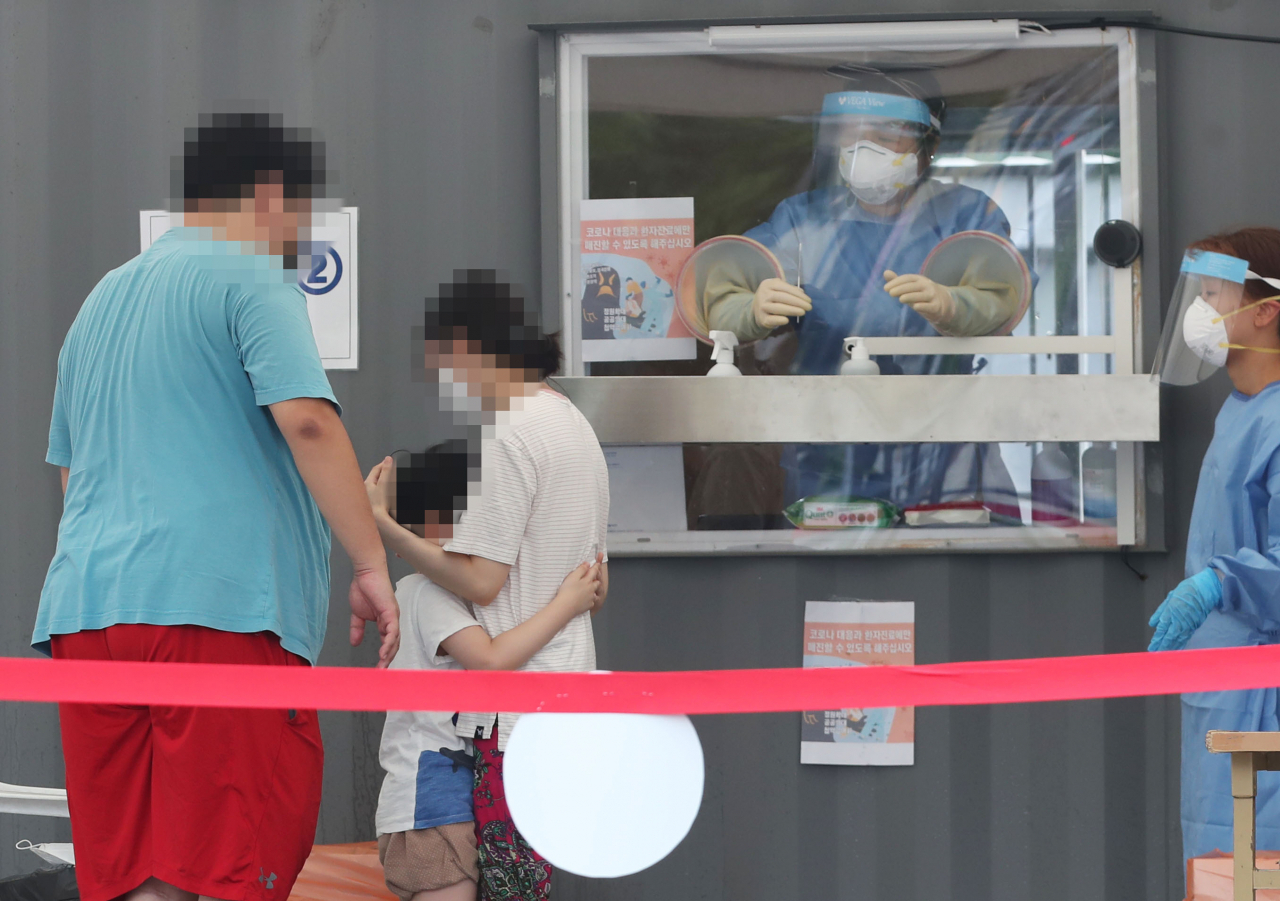 22일 오전 성북구청 앞 바람마당에 설치된 코로나19 선별진료소에서 한 아이가 검체 채취에 앞서 부모 품에 안겨있다. [연합뉴스]