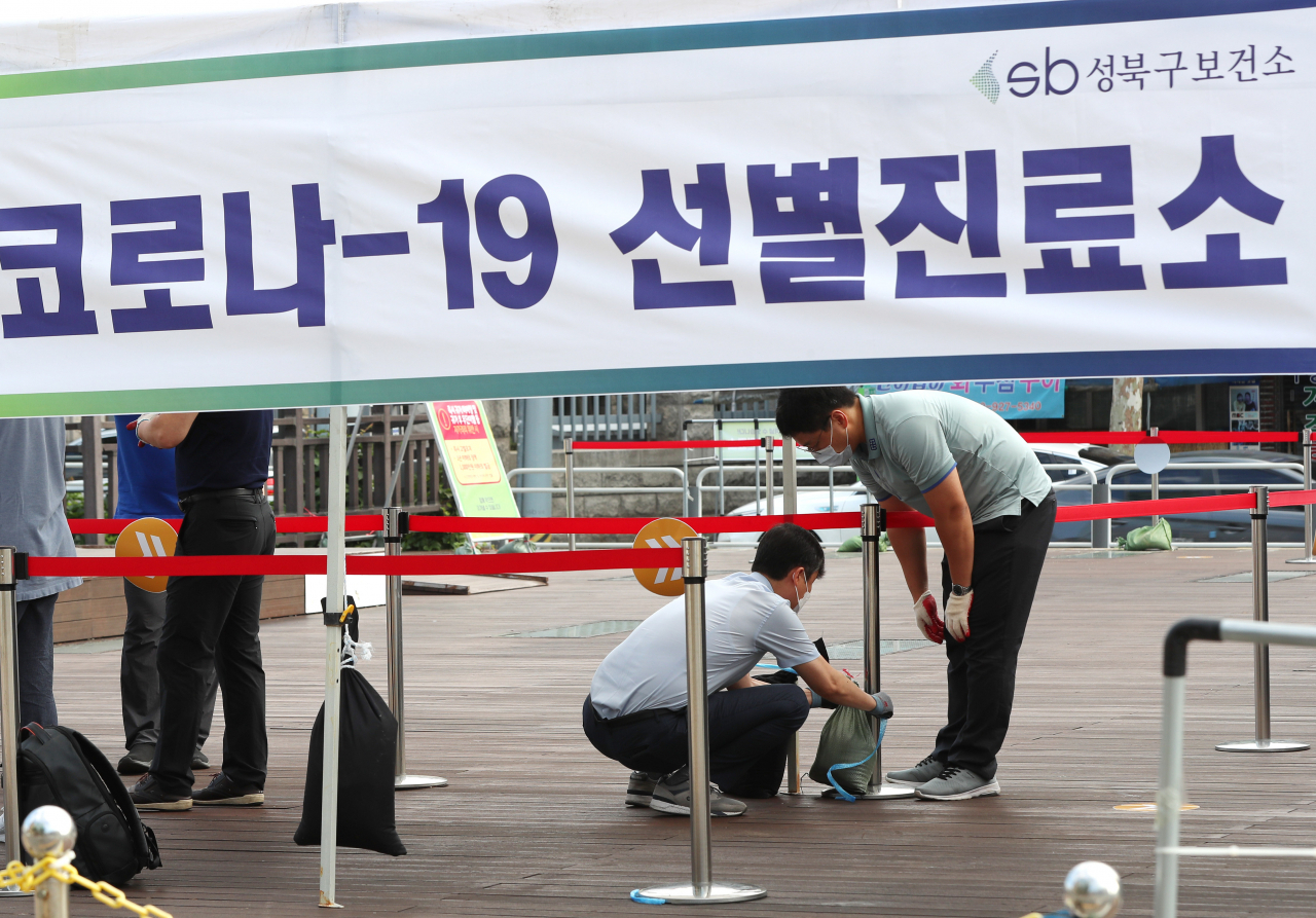 26일 오전 서울 성북구청 앞 바람마당에 설치된 코로나19 선별진료소에서 구청 직원들이 강풍에 대비해 모래주머니를 매달고 있다. 연합뉴스