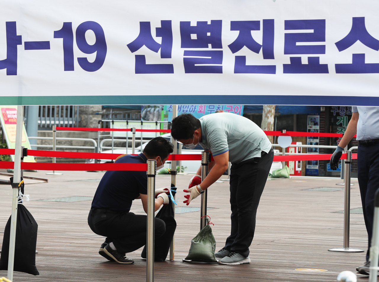 26일 오전 서울 성북구청 앞 바람마당에 설치된 코로나19 선별진료소에서 구청 직원들이 강풍에 대비해 모래주머니를 매달고 있다. [연합]