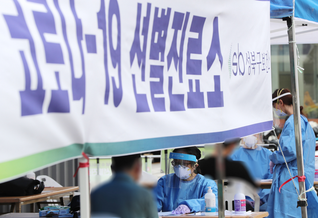 27일 오후 서울 성북구청 앞 바람마당에 설치된 코로나19 선별진료소에서 시민들이 검체 채취를 받기 전 문진표를 작성하고 있다. [연합]