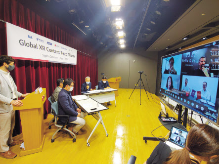 이상민 LG유플러스 부사장(착석자 4명 중 우측에서 2번째)이 화상회의를 통해 XR 얼라이언스 회원사들에게 인사말을 전하는 모습. TV화면 좌측 위부터 시계방향으로 KDDI, 펠릭스 앤 폴 스튜디오, 차이나텔레콤, 벨 캐나다 관계자.  [LG유플러스 제공]