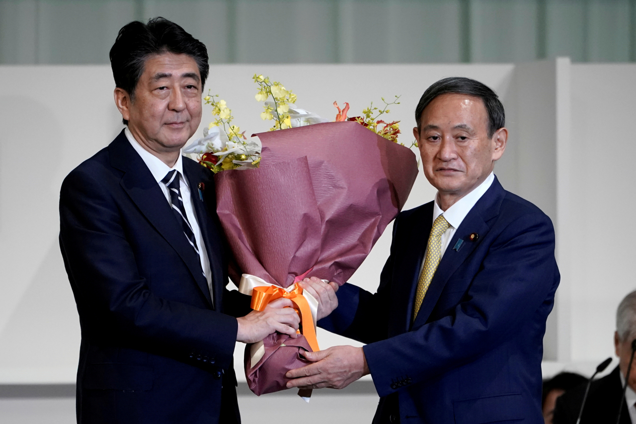 14일 일본 집권 자민당의 새로운 총재로 당선된 스가 요시히데(菅義偉) 관방장관(오른쪽)이 16일 임기를 마치는 아베 신조 총리에게 꽃다발을 선물하고 있다. [로이터]