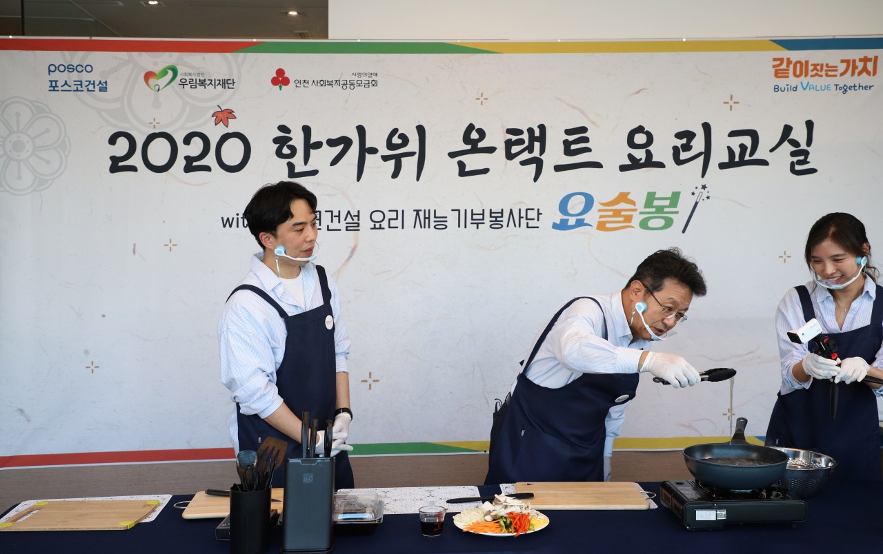 포스코건설 한성희 사장(사진 가운데)과 요리재능기부봉사단이 함께 유튜브로 추석요리 만들기 시범을 보이고 있다. [포스코건설 제공]