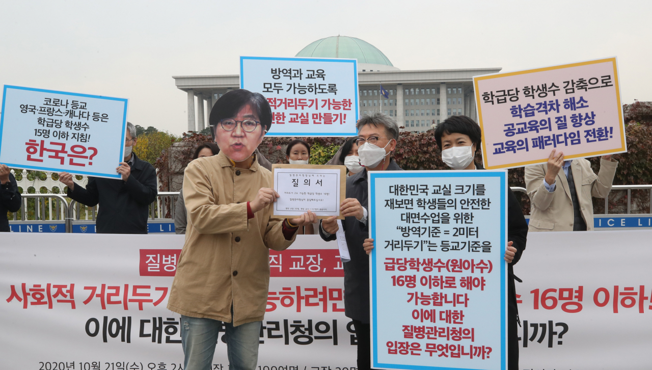 현직 교장 및 교사들이 지난해 10월21일 오후 국회 정문 앞에서 ‘사회적 거리두기 2m - 학급당 학생 수 16명을 촉구한다’ 기자회견을 하고 있는 모습. 이들은 “사회적 거리두기 2m를 유지하면서 등교 수업을 하려면, 3분의1 등교나 3분의2 등교라는 기준이 아니라, 학급당 학생수 16명 이하이어야 한다”며 정은경 질병관리청장에게 질의하는 퍼포먼스를 했다. [연합]
