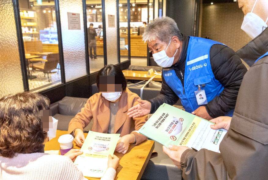 An official from Yancheon-gu, western Seoul, briefs on the face mask mandate to visitors at a cafe in the district on Friday. (Yangchen-gu)