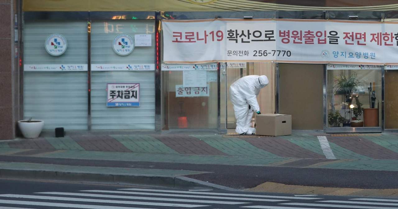 10일 오후 신종 코로나바이러스 감염증(코로나19) 확진자 43명이 추가돼 하루에만 47명이 확진 판정을 받은 울산시 남구 양지요양병원 앞에서 방호복을 입은 병원 관계자가 문 밖에 놓인 물품을 안으로 옮기고 있다. [연합]