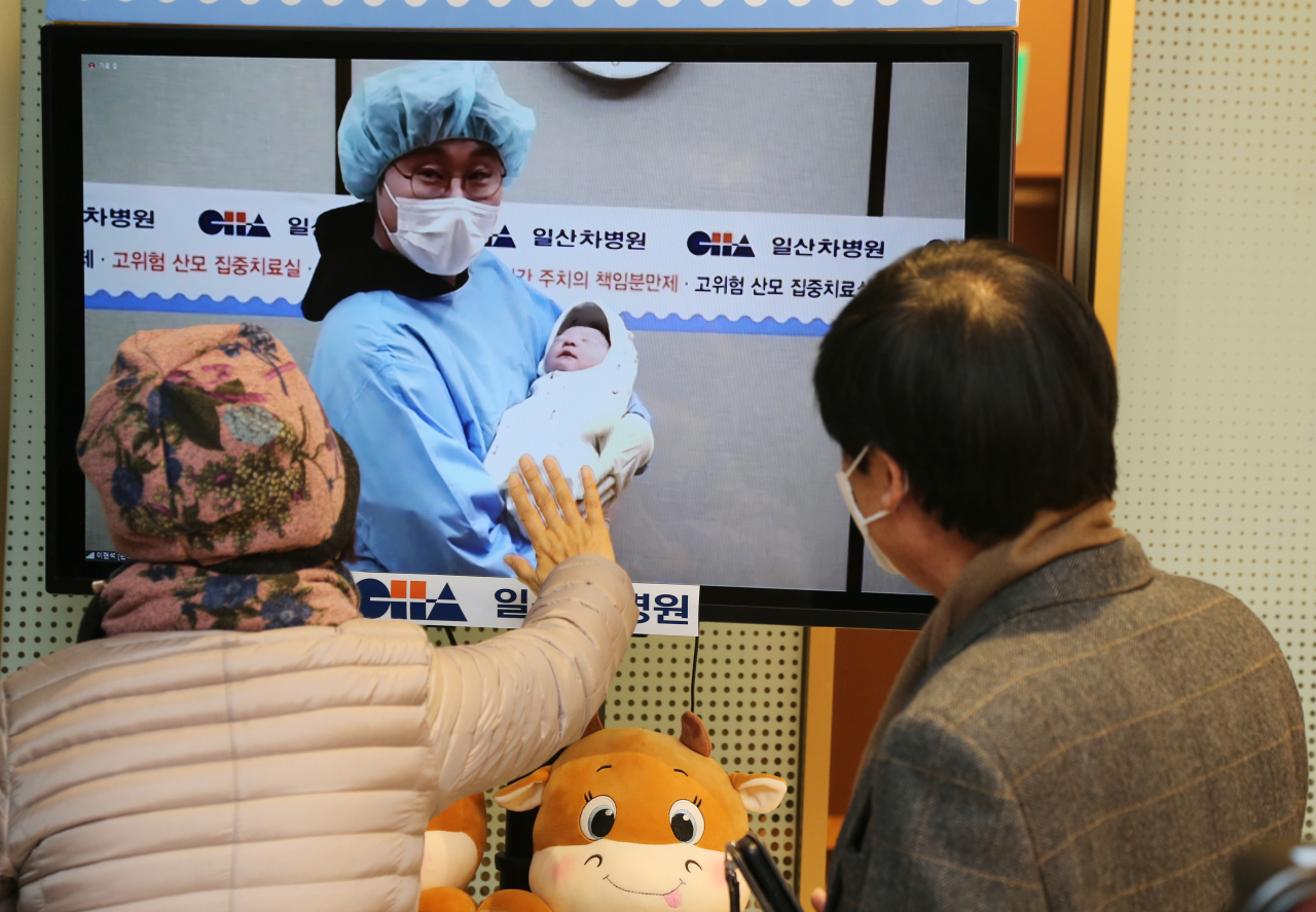 경기도 고양시 일산차병원에서 2021년 1월 1일 0시 0분 태어난 임상현(36)·정송민(34) 씨의 아들(3.43㎏)이 아빠 품에 안겨 있다. 신종 코로나바이러스 감염증(코로나19) 탓에 나머지 가족들이 외부에 설치된 TV화면을 통해 생중계로 '새해 첫 아기' 탄생의 기쁨을 함께하고 있다. [연합]