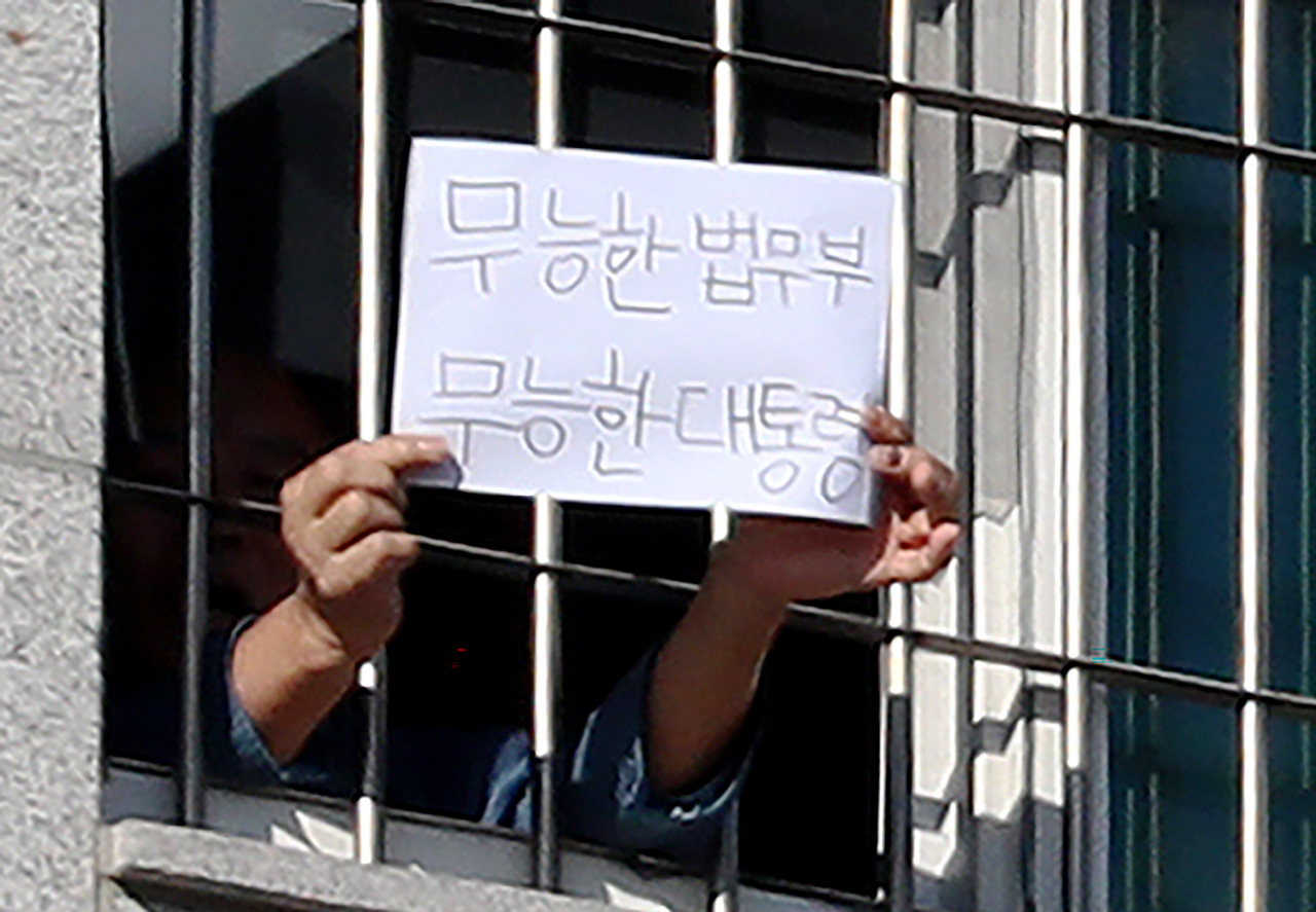 6일 오후 서울 송파구 동부구치소에서 한 수용자가 '무능한 법무부 무능한 대통령'이라고 쓴 종이를 창문 밖 취재진에게 내보이고 있다. [연합]