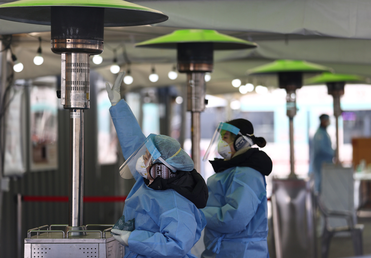 Medical workers warm their hands at heaters set up around a temporary coronavirus screening center in front of Seoul Station on Sunday, during a strong cold wave sweeping across South Korea. (Yonhap)