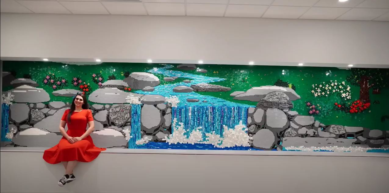 레고아티스트 제시카 이우드 씨가 미국의 ASML 윌튼 지사에 설치된 ‘고요한 자외선 폭포’(Serene Ultraviolet Waterfall)’ 작품과 기념촬영을 하고 있다. 이 작품은 총 7만개가 넘는 브릭이 투입됐고, 조립기간만 2개월이 소요됐다. [ASML 뉴스룸]