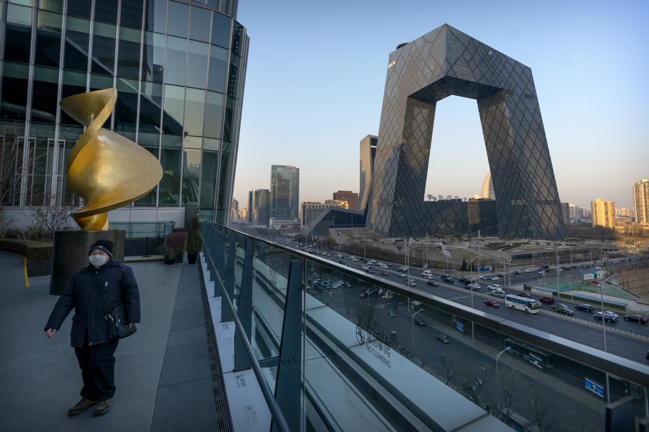 A man wearing a face mask to protect against the spread of the coronavirus walks along an observation deck near the CCTV Headquarters building, the home of Chinese state-run television network CCTV and its overseas arm CGTN, in Beijing, Thursday, Feb. 4, 2021. (AP Photo