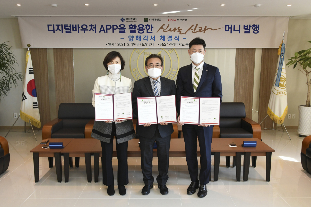 BNK부산은행은 19일 오후 신라대학교 대학본부에서 신라대학교, 부산광역시와 ‘디지털바우처 앱(APP)을 활용한 ‘신나는 신라머니’ 발행 업무협약을 체결했다.(사진 오른쪽부터 부산은행 이주형 디지털금융본부장, 신라대학교 김충석 총장, 부산광역시 정나영 스마트시티 추진과장)[부산은행 제공]