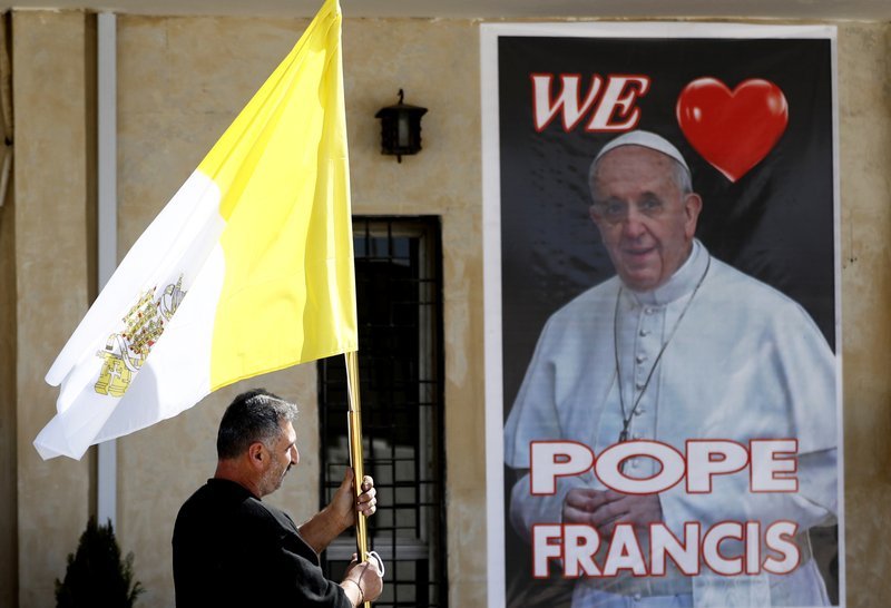 A Christian priest holds a Vatican flag as he walks by a poster of Pope Francis during preparations for the Pope’s visit in Mar Youssif Church in Baghdad, Iraq, Friday. (AP-Yonhap)