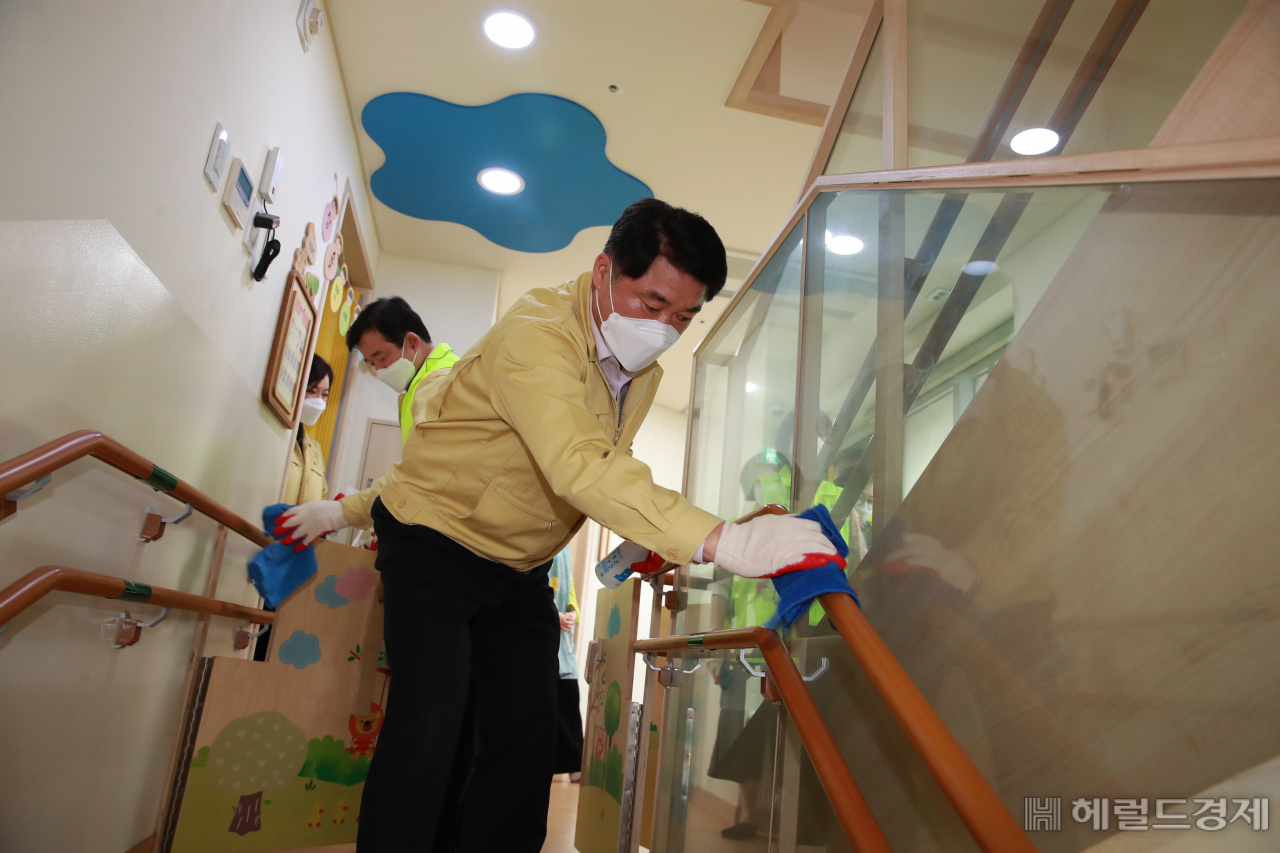 박준희 관악구청장이 지난달 31일 오후 어린이집을 찾아 알콜수건으로 어린이들이 손을 잡고 계단을 오르는 안전봉을 소독하고 있다. [관악구 제공]