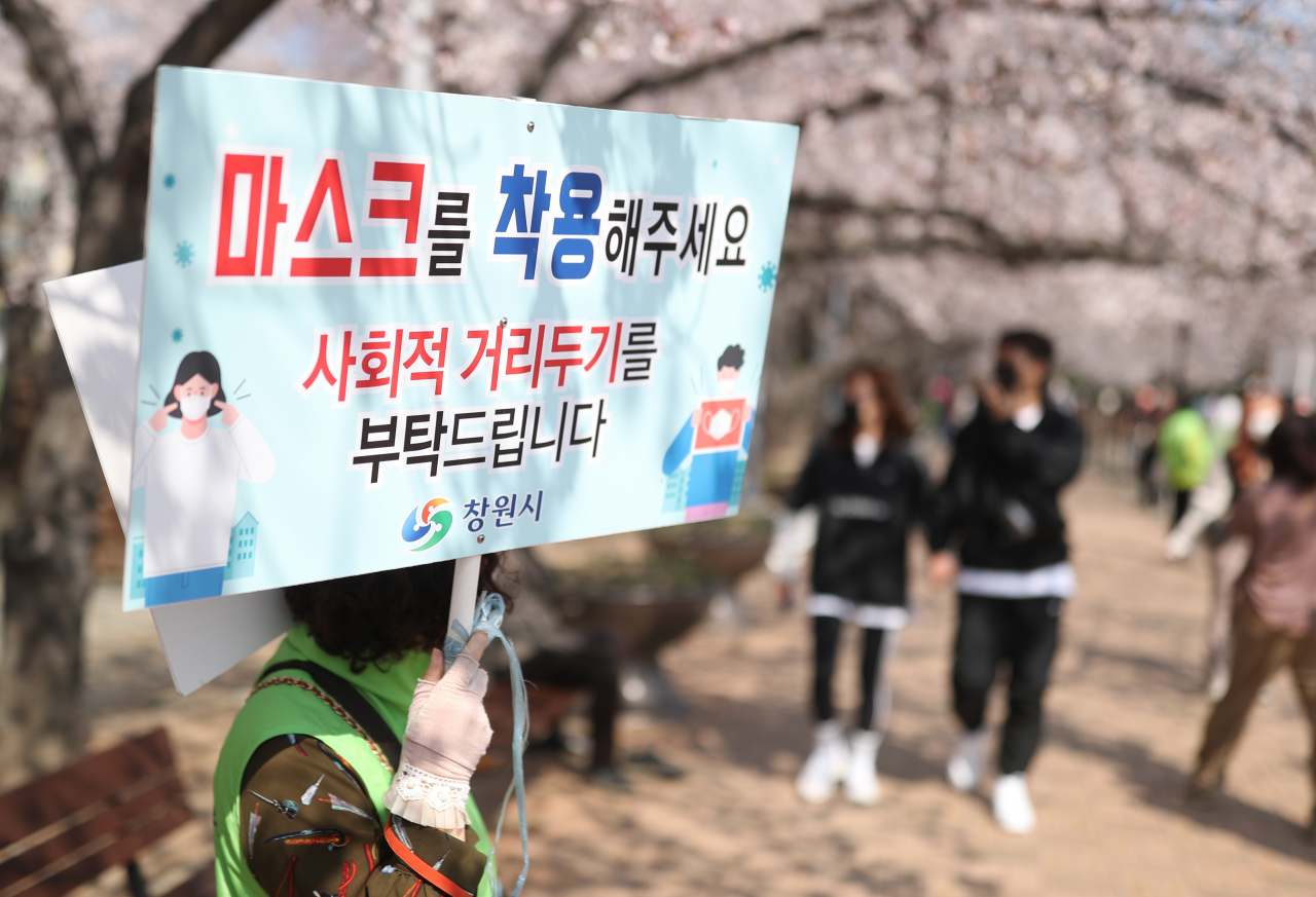 코로나19 여파로 마스크 착용과 사회적 거리두기 강화 등 일상 속 생활방역으로 인해 호흡기질환 입원율이 낮아졌다는 연구 결과가 국내 연구진에 의해 발표됐다. 지난 25일 경남 창원시 진해구 경화역공원에서 창원시 관계자가 ‘마스크 착용’ 협조 팻말을 들고 있다. 창원시는 상춘객이 몰릴 것을 염려해 지난해에 이어 올해도 전국 최대규모 벚꽃 축제인 진해 군항제를 취소했다. [연합]