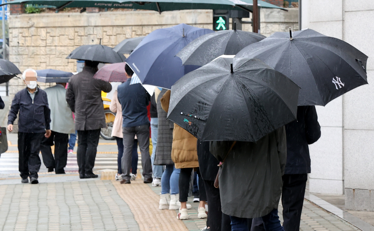 지난 12일 오후 서울 중랑구 보건소에 마련된 코로나19 임시선별진료소를 찾은 시민들이 우산을 쓰고 순서를 기다리고 있다. [연합]