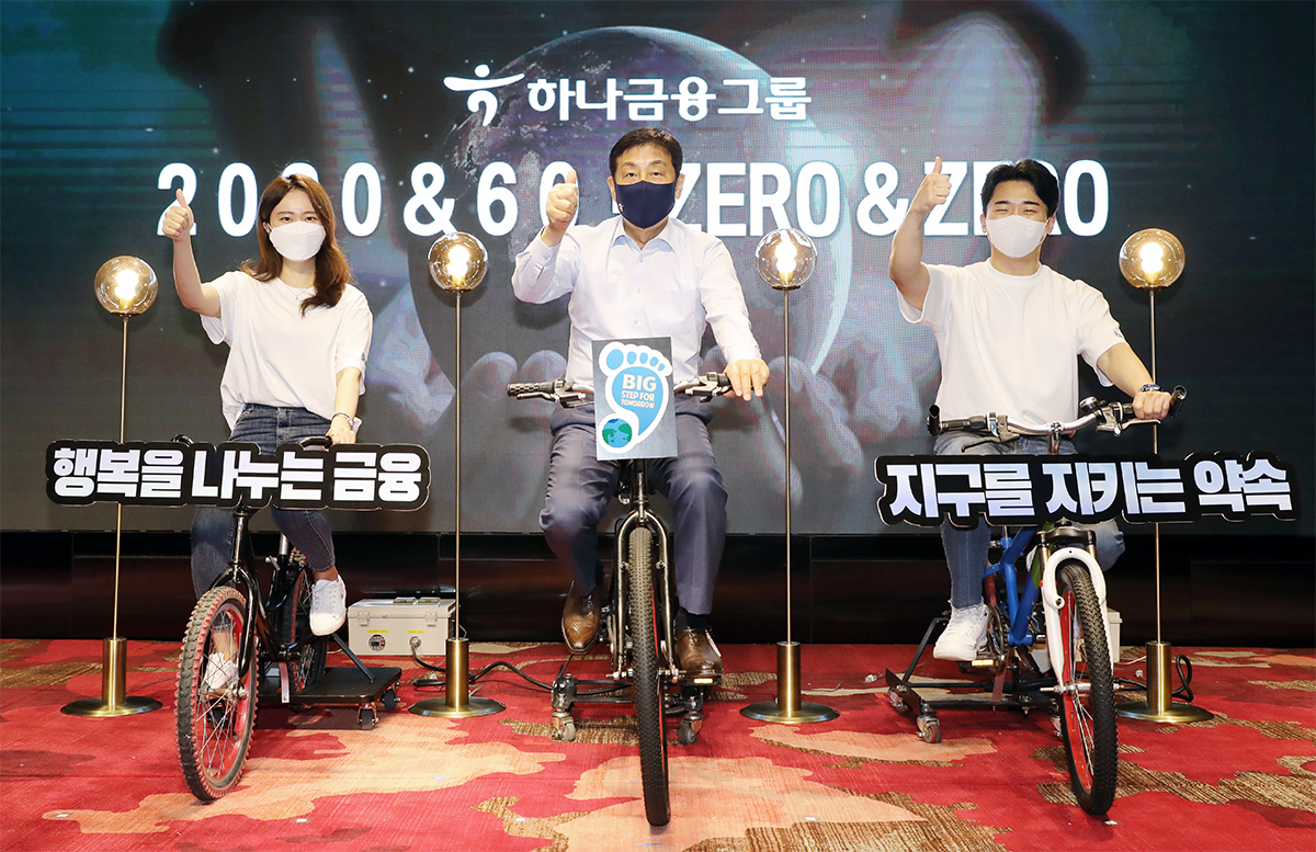 Hana Financial Group Chairman Kim Jung-tai (center) pedals a stationary bicycle linked to a dynamo at a ceremony held to announce the group‘s new ESG financing goals in Seoul on Thursday.(Hana Financial Group)