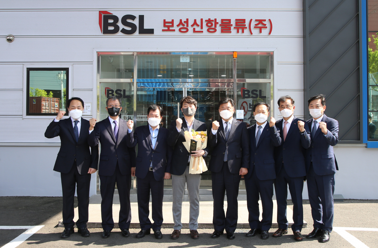 BNK경남은행 최홍영 은행장(사진 오른쪽 네번째)이 보성신항물류㈜ 최병목 상무(사진 왼쪽 네번째)에게 표창패와 꽃다발을 수여한 뒤 기념촬영 하고 있다.