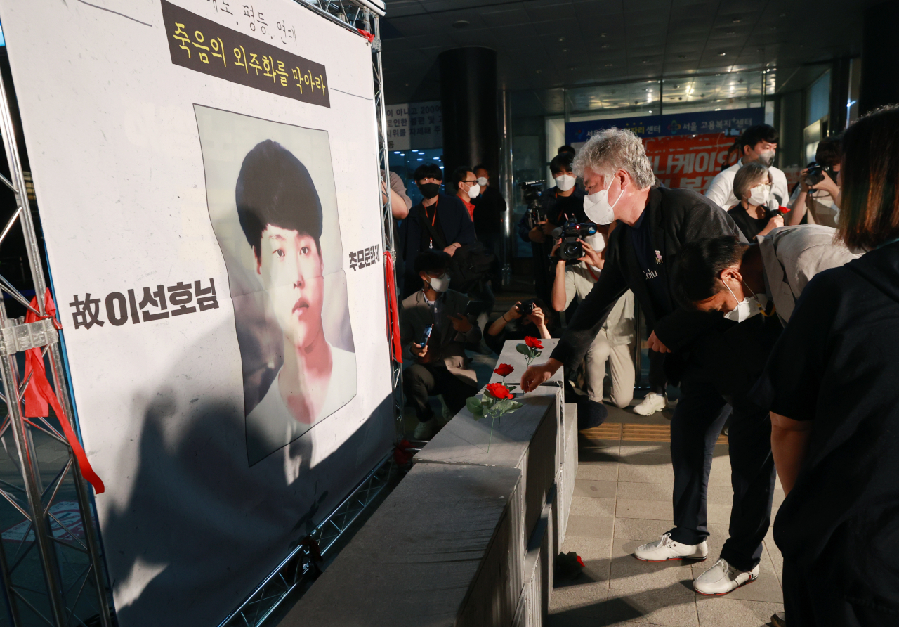 평택항에서 일하다 사고로 숨진 20대 청년 노동자 고(故) 이선호 씨의 부친 이재훈 씨가 13일 오후 서울 중구 서울지방고용청 앞에서 열린 추모문화제에서 아들의 얼굴이 새겨진 현수막 앞 컨테이너 모형에 추모의 꽃을 꽂고 있다. [연합]