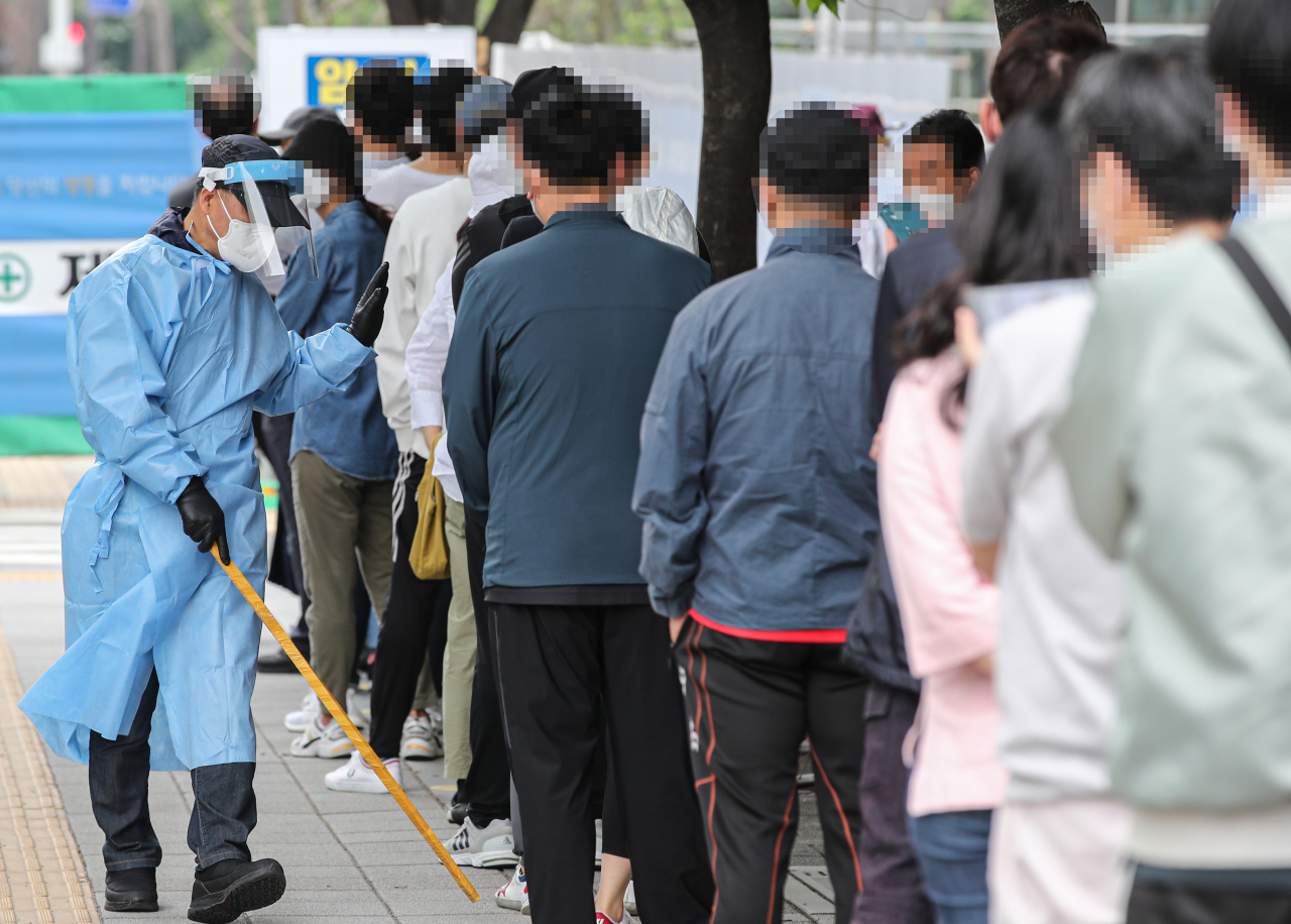 신종 코로나바이러스 감염증(코로나19) 신규 확진자가 연이틀 500명대를 기록한 29일 오전 서울시 송파구 보건소 선별진료소에서 관계자가 검사를 받기 위해 줄지어 서 있는 시민들에게 거리 두기를 안내하고 있다.[연합]