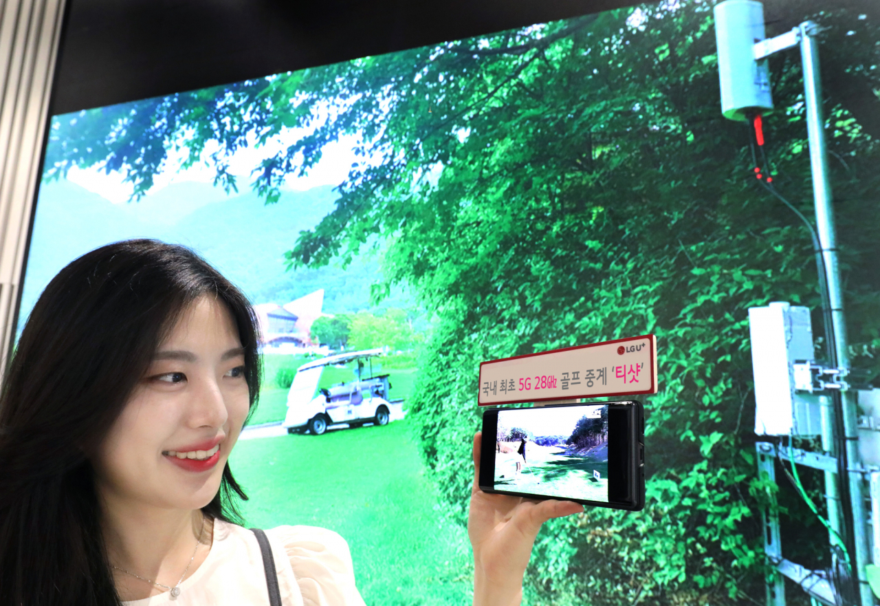 LG유플러스가 국내 최초로 5G 28㎓ 기반의 중계 콘텐츠를 선보인다고 16일 밝혔다. 오는 20일까지 충북 음성군 레인보우힐스CC에서 열리는 ‘DB그룹 제35회 한국여자오픈 골프선수권대회’를 ‘U+골프’에서 5G 28㎓ 네트워크를 활용해 중계한다. LG유플러스 모델이 레인보우힐스CC에 구축된 5G 28㎓ 기지국 현장 사진을 배경으로 U+골프 서비스를 감상하는 모습. [LG유플러스 제공]