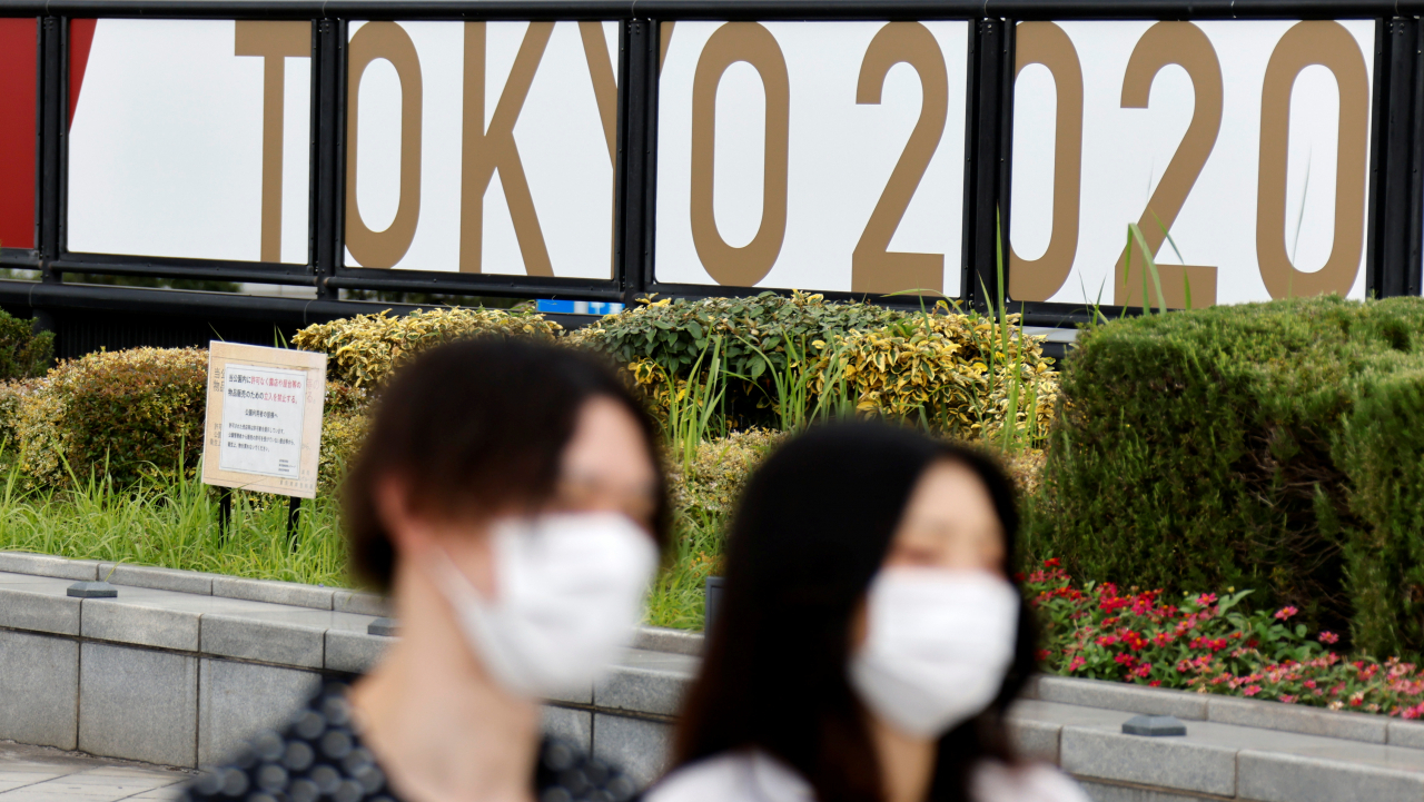 지난 27일 일본 도쿄에 위치한 2020 도쿄올림픽 광고판 앞을 마스크를 쓴 시민들이 지나가고 있다. [로이터]