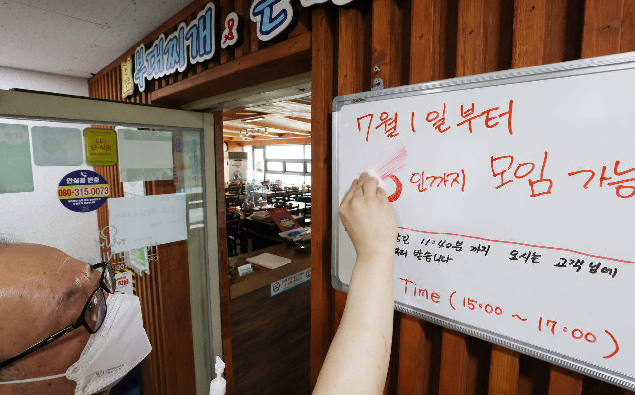 지난달 30일 오후 서울의 한 음식점 관계자가 '다음달부터 6인까지 모임 가능' 안내 문구를 삭제하고 있다. [연합]