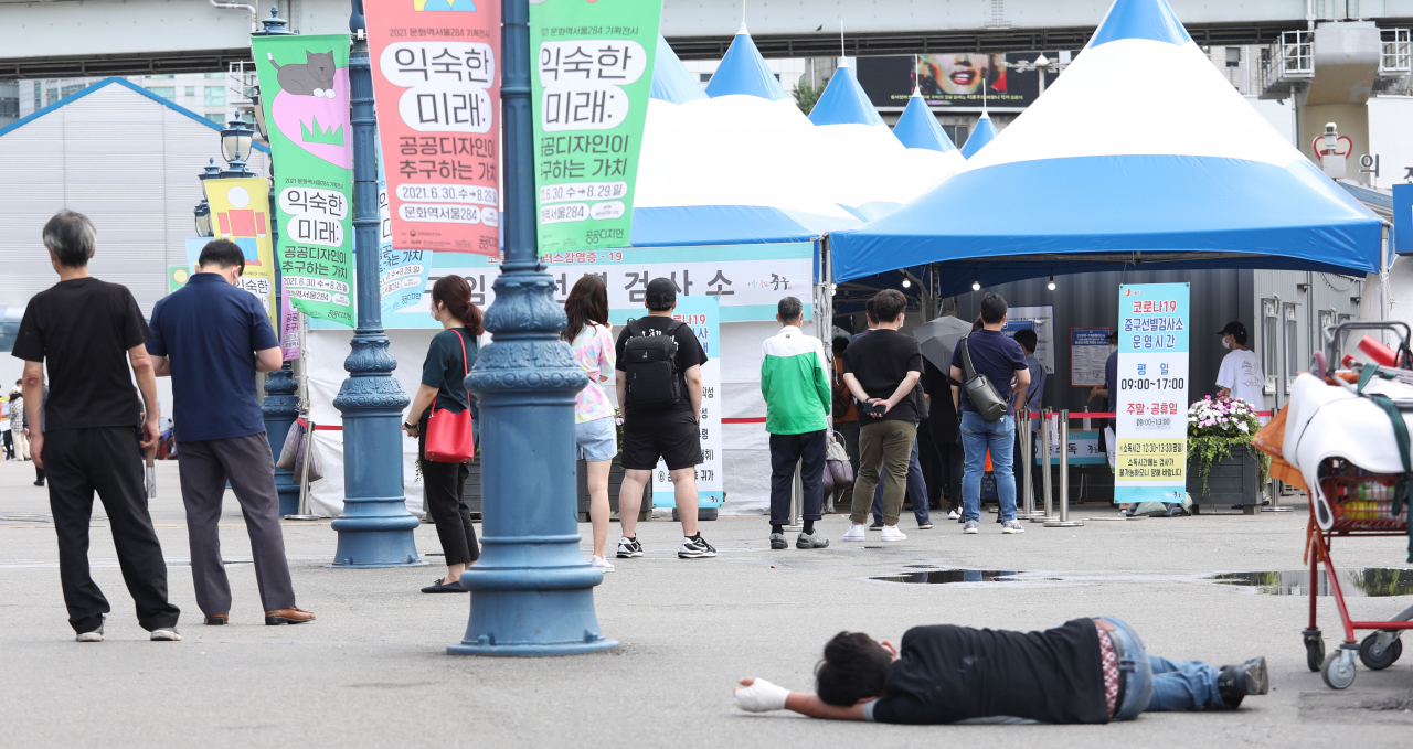 14일 서울역 임시선별진료소에서 시민들이 검사를 기다리고 있다. 그 옆에 한 노숙인이 누워 있다. 중앙방역대책본부는 이날 0시 기준 신규 확진자가 전날보다 465명 늘어난 1천615명이라고 밝혔다. 연합뉴스