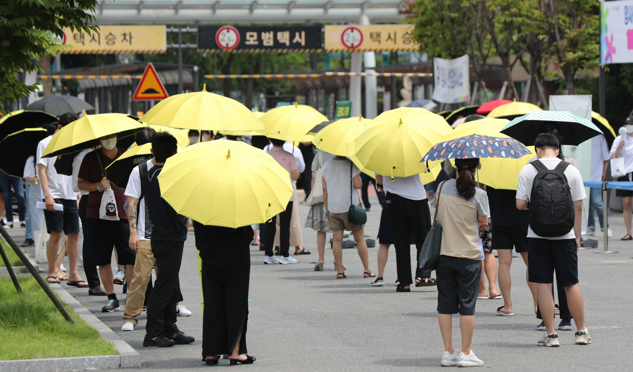 국내 신종 코로나바이러스감염증(코로나19) 신규 확진자 수가 역대 최다를 기록한 14일 오후 서울 서초구 고속버스터미널 광장에 마련된 임시선별검사소 앞에서 서초구가 마련한 양산을 빌려 쓴 시민들이 검사 순서를 기다리고 있다. [연합]