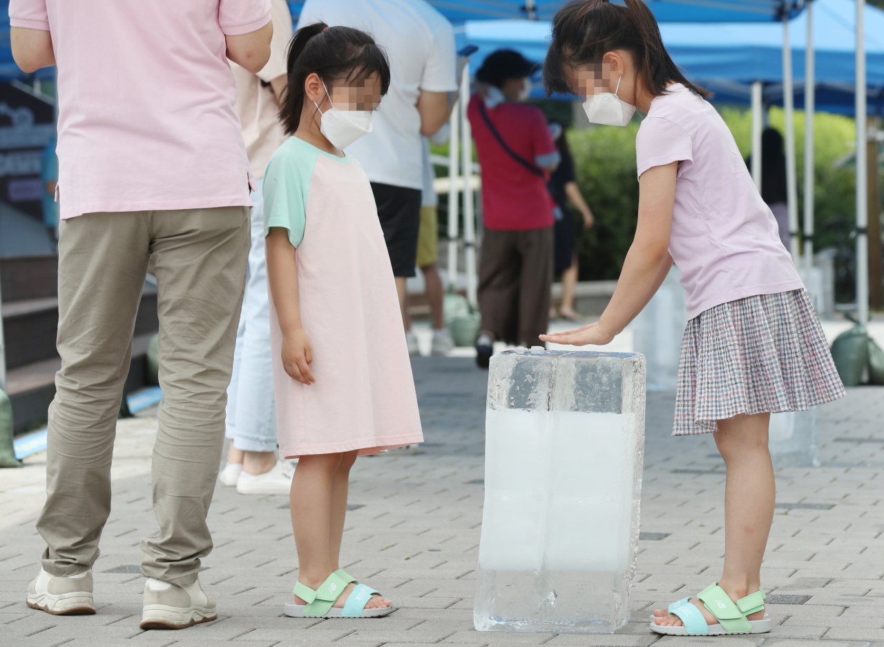 지난 19일 오전 부모와 함께 서울 관악구 코로나19 선별검사소를 찾은 어린이들이 얼음의 내뿜는 냉기에 더위를 식히고 있다. [연합]