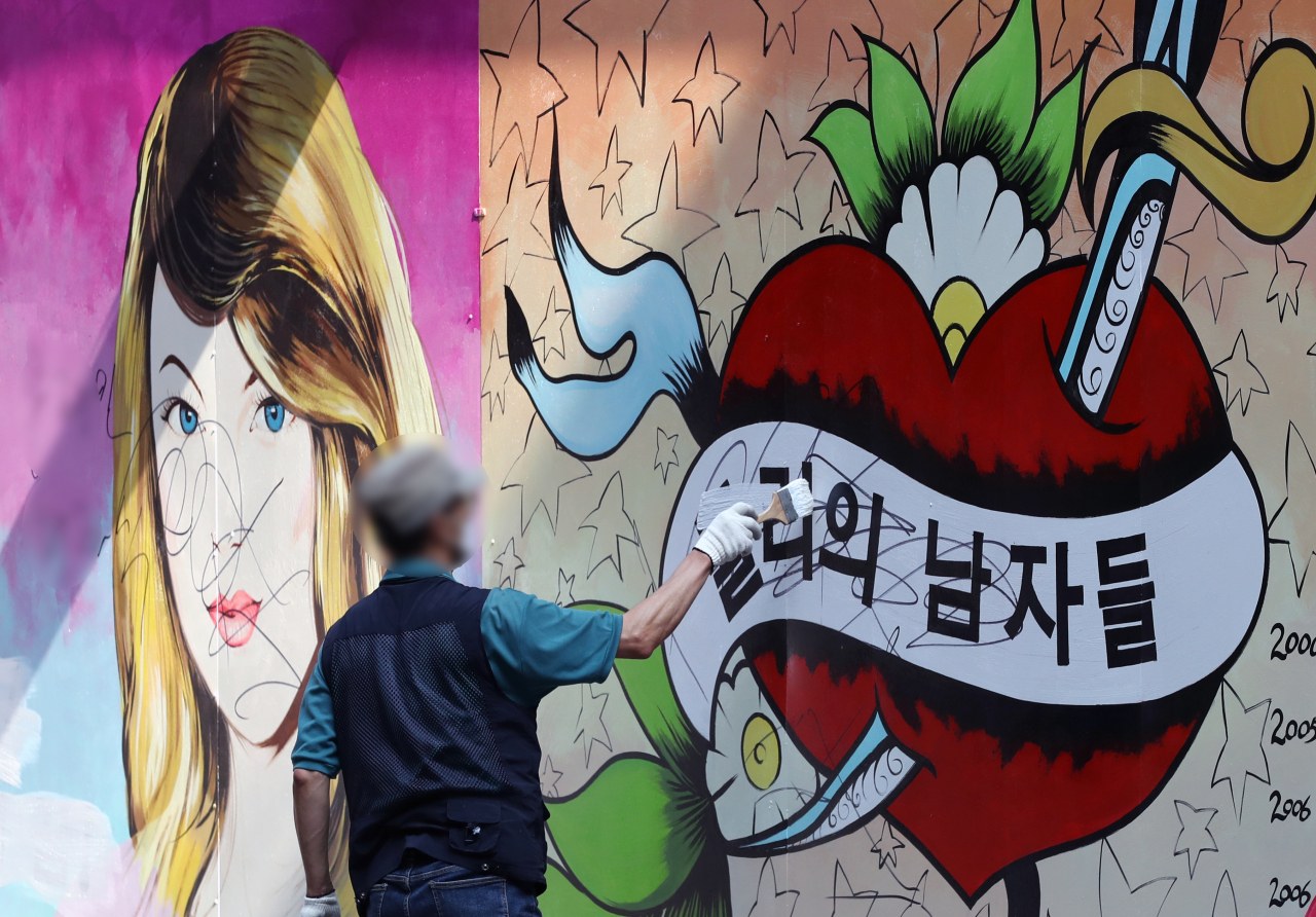 서울 종로구의 한 중고 서점 외벽에 그려진 대선주자인 윤석열 전 검찰총장의 부인 김건희 씨를 빗대 비방하는 듯한 내용의 벽화가 논란이 되는 가운데 30일 오전 건물 관계자가 벽화의 글자를 흰색 페인트로 칠하고 있다. [연합]