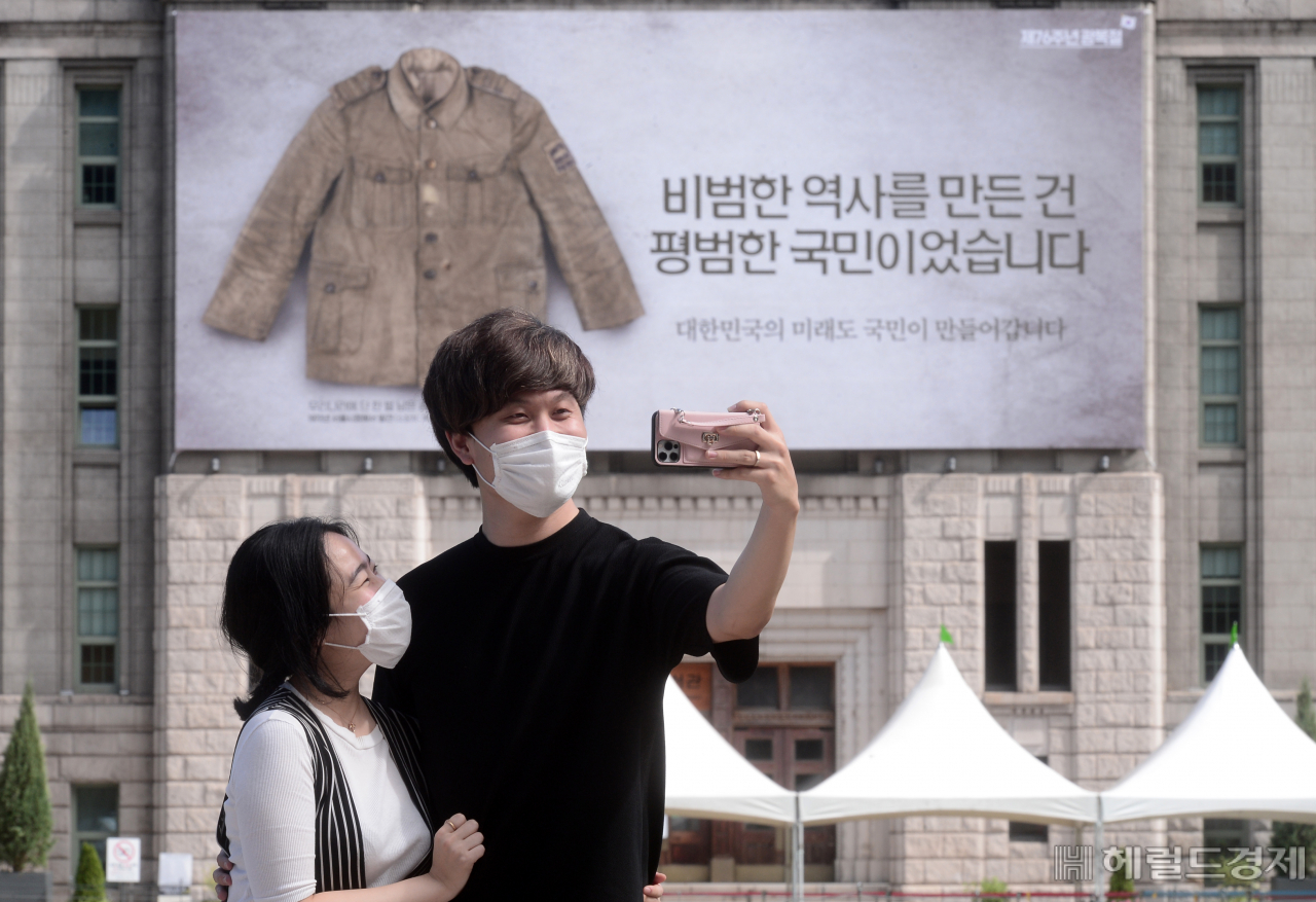 9일 오전 서울광장에 마련된 꿈새김판에 ‘비범한 역사를 만든 건, 평범한 국민이었습니다. 대한민국의 미래도 국민이 만들어갑니다’ 라는 문구가 담긴 광복군 군복 사진 아래에서 한 커플이 기념 셀카를 찍고 있다. 서울시는 오는 15일 제76주년 광복절을 전후해 총 3편의 광복절 기념 꿈새김판을 연속으로 게시한다고 밝혔다. 박해묵 기자/mook@heraldcorp.com