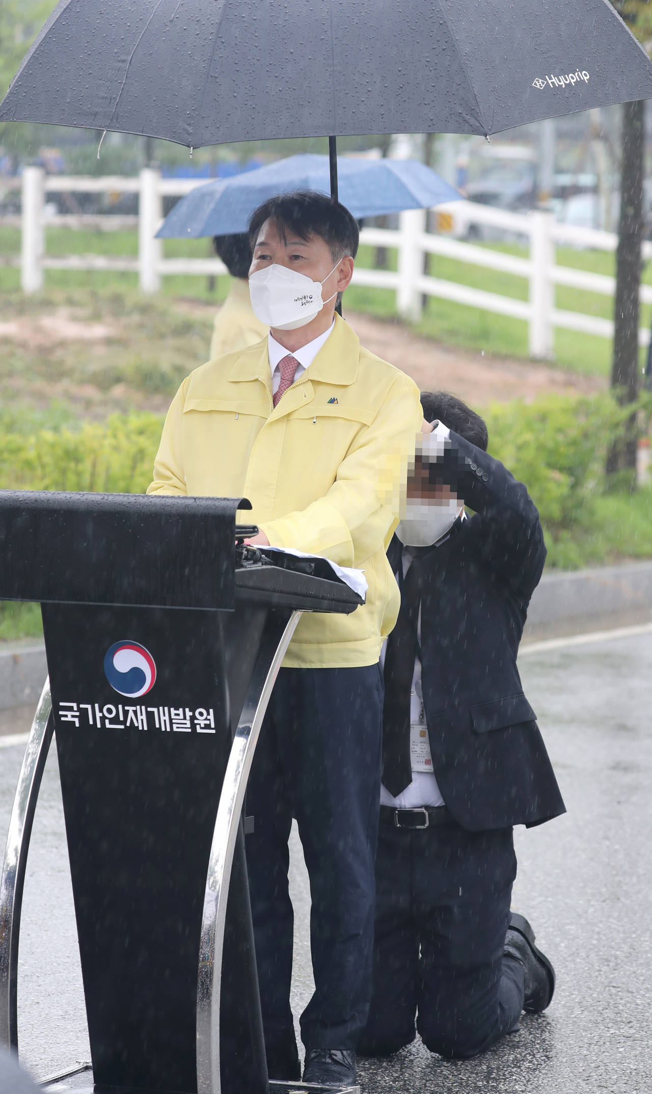 강성국 법무부 차관이 27일 충북 진천 국가공무원인재개발원에서 아프가니스탄 특별입국자 초기 정착 지원과 관련해 브리핑하는 도중 관계자가 뒤쪽에서 무릎을 꿇고 우산을 받쳐주고 있다. [연합]