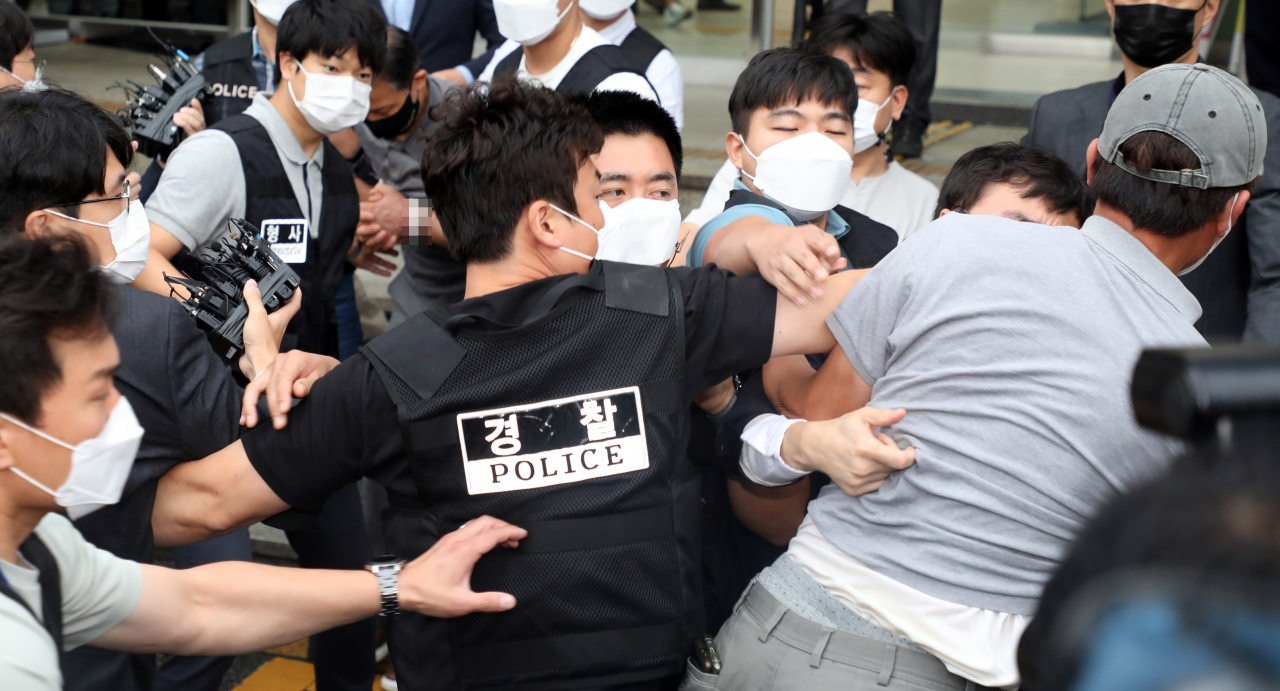 7일 오전 송파경찰서에서 전자발찌 훼손 전후로 여성 2명 살해 혐의로 이송되는 강윤성에게 유가족으로 보이는 한 남성(오른쪽 모자 쓴 사람)이 달려들자 경찰이 제지하고 있다. 송파경찰서는 이날 강씨를 서울동부지검에 송치했다. [연합]