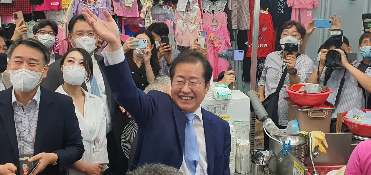 국민의힘 대권주자인 홍준표 의원이 10일 대구 서문시장을 찾아 노점에서 식사하다가 지지자들을 향해 손을 흔들고 있다. [연합]