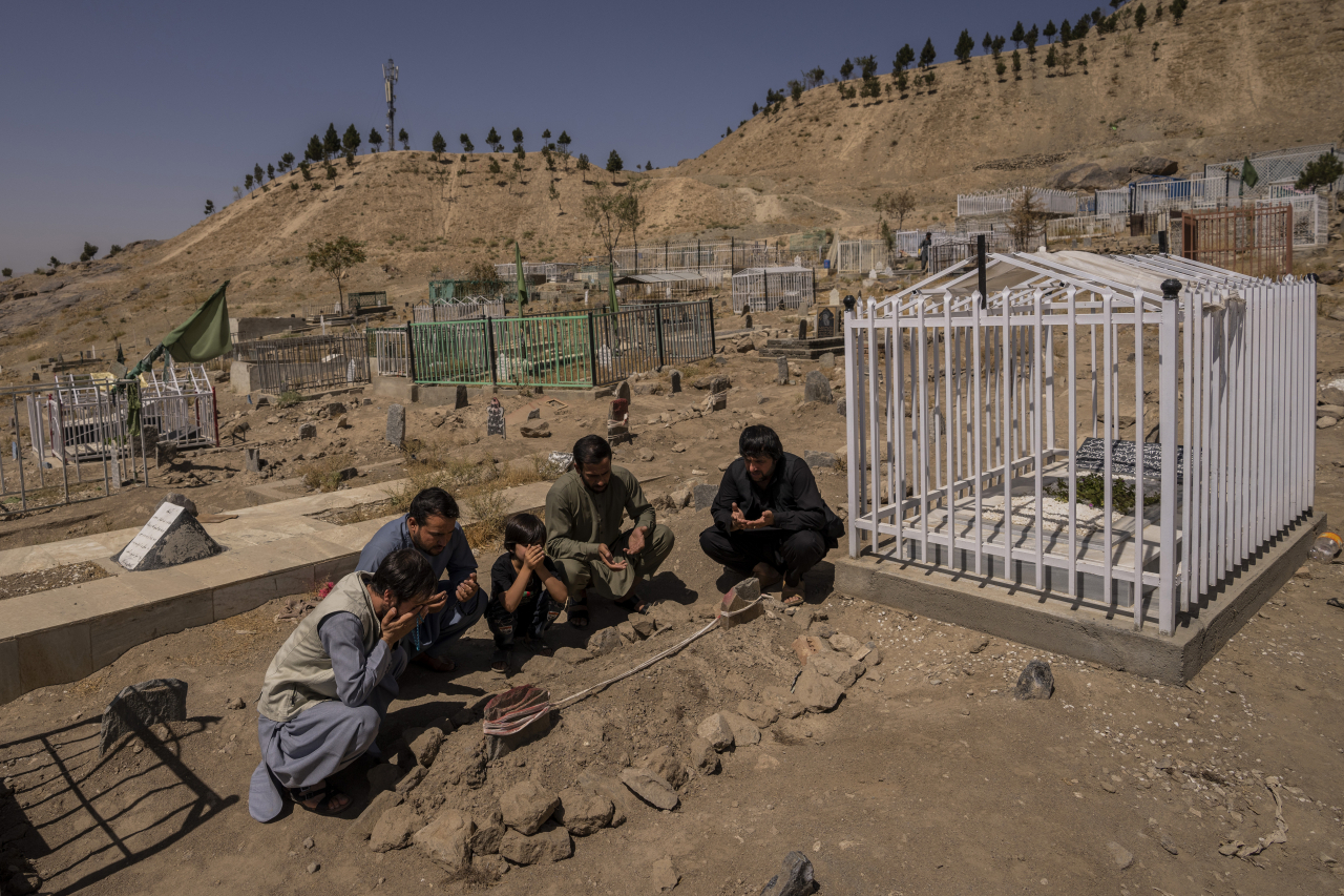 지난달 미국의 아프가니스탄 드론 공격으로 가족 10명을 잃은 에말 아흐마디와 유족이 희생한 가족 무덤 옆을 지키고 있는 모습. [AP]