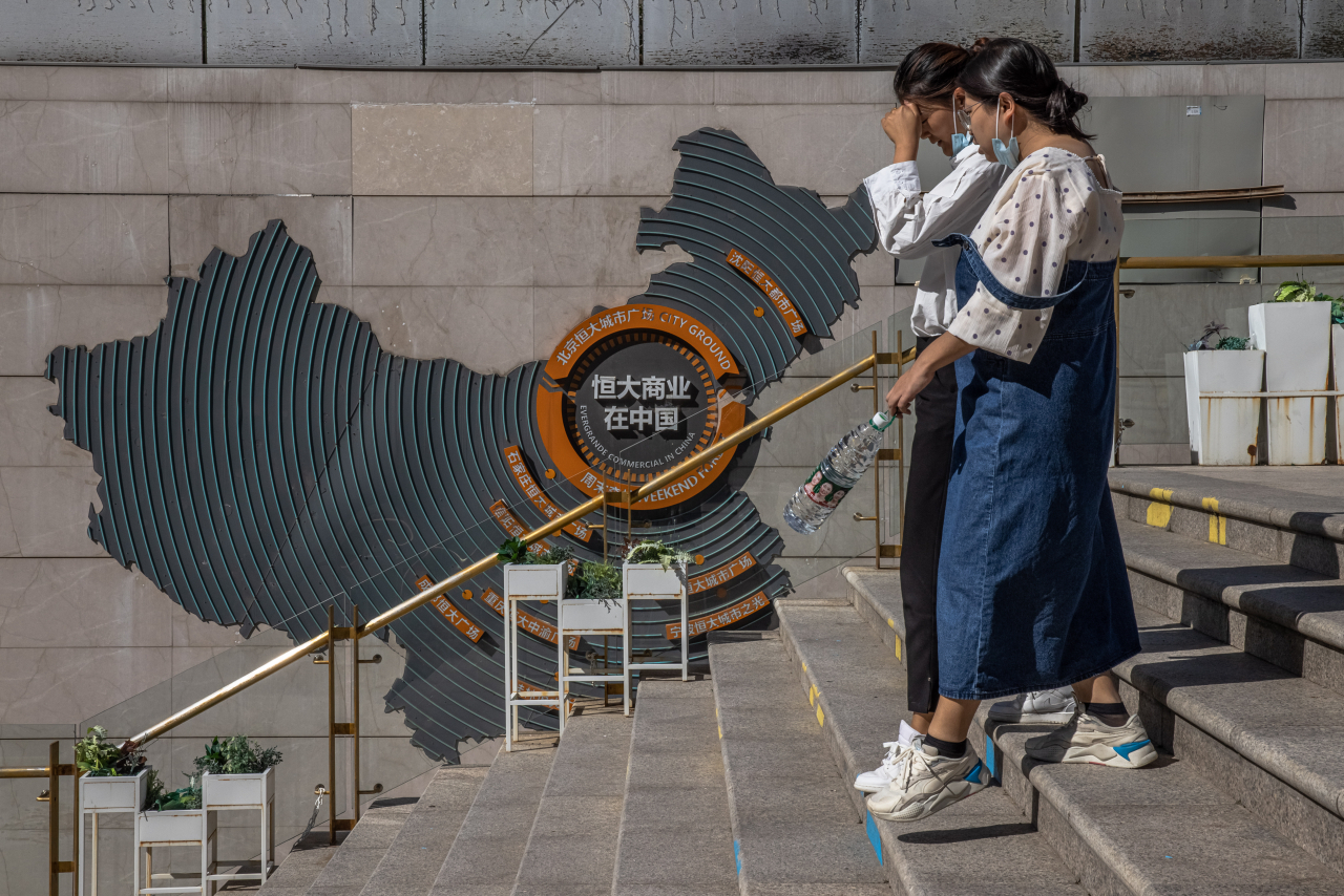 22일(현지시간) 중국 베이징(北京) 헝다(恒大·에버그란데)그룹 시티 플라자 계단에 헝다그룹의 개발 프로젝트를 설명하는 장식물이 설치된 벽을 시민들이 지나치고 있다. [EPA]