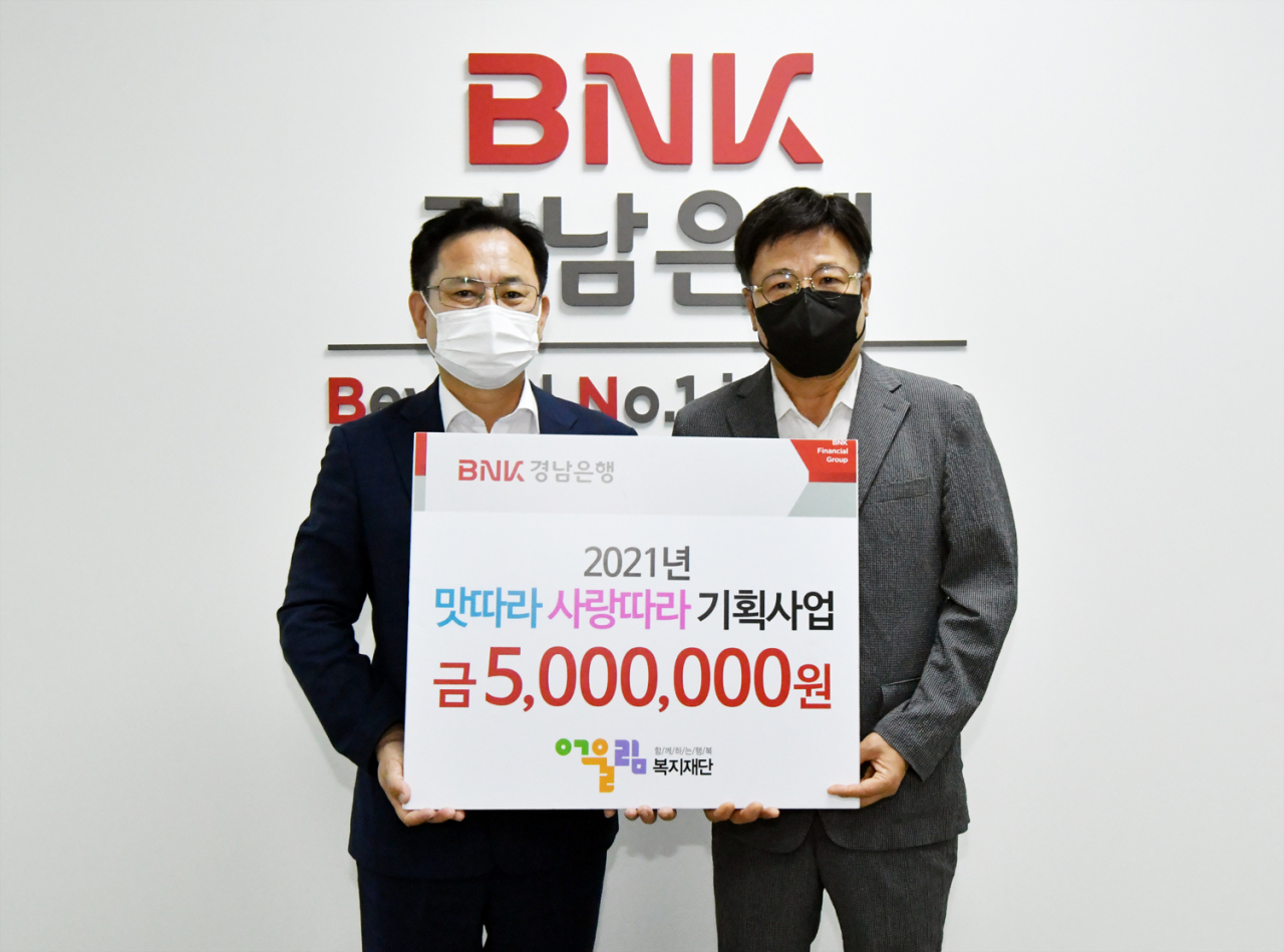 BNK경남은행 이상봉 상무가 (사)어울림복지재단 윤운룡 이사장에게 ‘맛따라 사랑따라 기획사업 기금 기탁 증서’를 전달하고 있다.