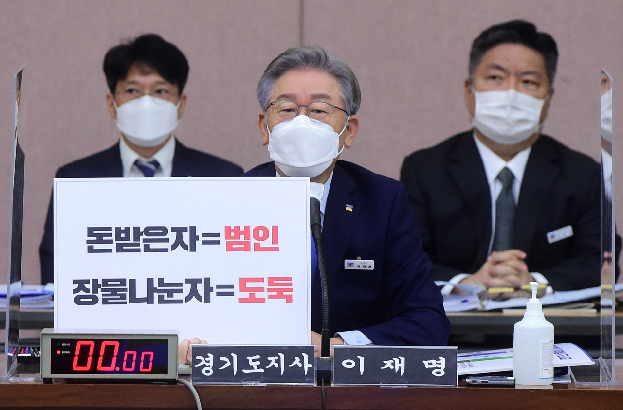 Gyeonggi Province Gov. Lee Jae-myung attends the parliamentary audit at the province government office in Suwon, Gyeonggi Province on Monday. The placard reads “recipient of money = culprit, sharer of stolen property = thief,” in an implicit denial of allegations surrounding a land development project in Seongnam, Gyeonggi Province. (Yonhap)