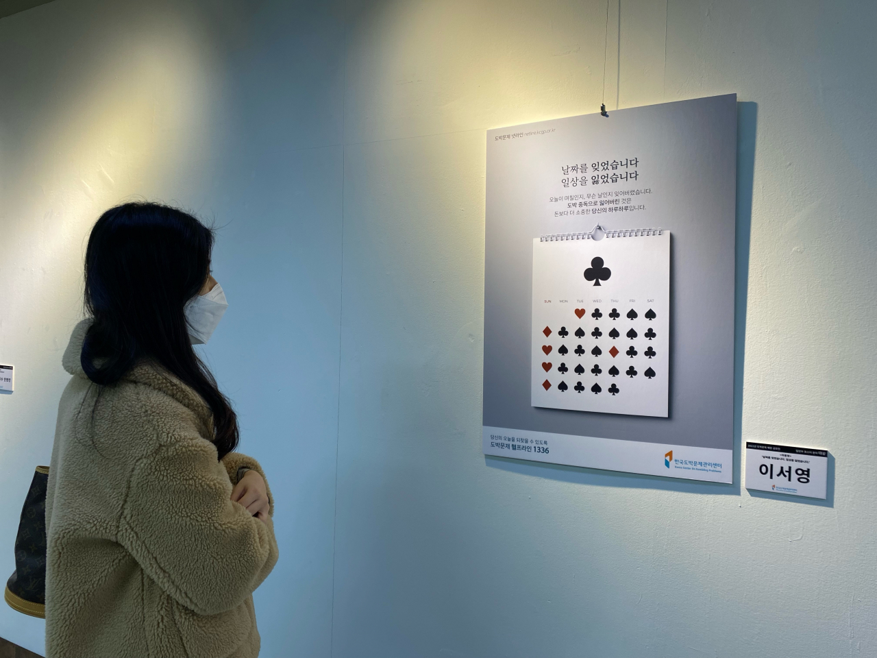 18일 을지로 아뜨리애 갤러리를 방문한 시민이 포스터 ‘날짜를 잊었습니다. 일상을 잃었습니다’를 보고 있다. 본 포스터를 창작한 이서영 작가는 도박으로 물든 일상을 달력과 카드 이미지로 감각적으로 표현해 ‘2021년 도박문제 예방 공모전’의 일반부 포스터 부문 대상을 수상했다. [한국도박문제관리센터 제공]