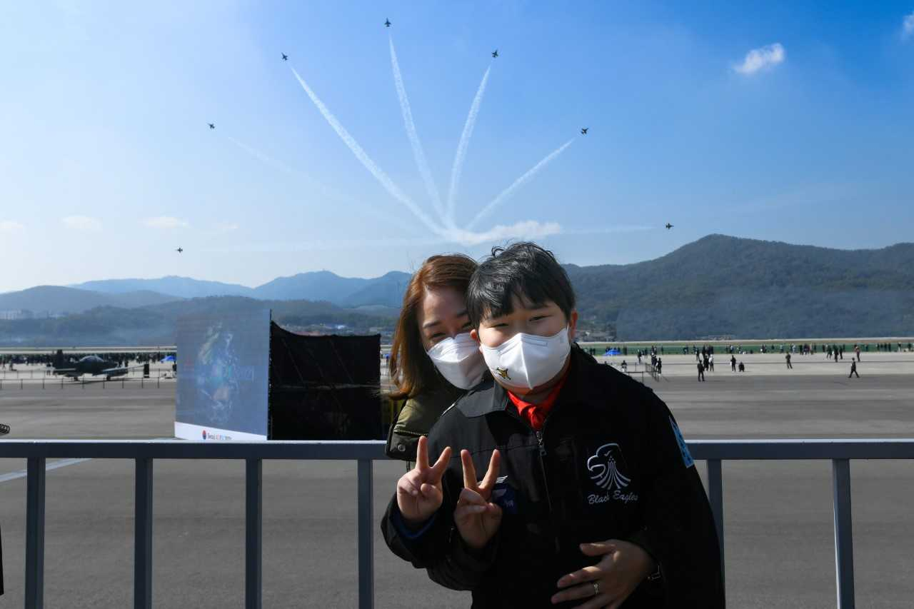 공군 특수비행팀 블랙이글스는 22일 ‘서울 ADEX 2021’이 진행 중인 서울공항에서 희귀 소아암으로 투병 중인 최윤수 군을 초청해 특별 이벤트를 마련했다. 이날 행사에 참석한 최윤수 군이 블랙이글스 에어쇼를 관람하는 도중 어머니와 함께 기념촬영을 하고 있다. [공군 제공]